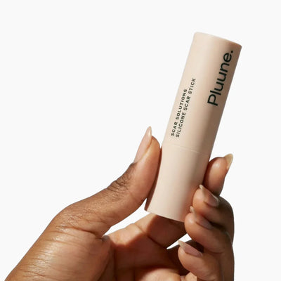 Hand holding Pluune Scar Solutions silicone scar stick on white background